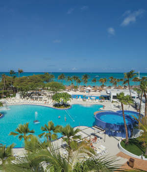 Aerial view of Hotel Riu Palace Antillas, showcasing a large pool area with palm trees and ocean in the background.