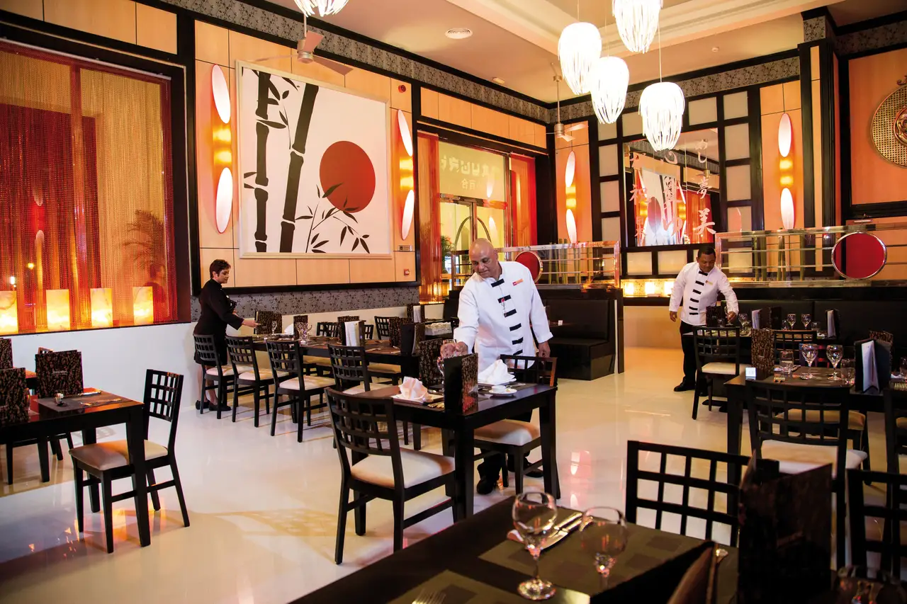 Elegant Japanese restaurant in Hotel Riu Palace Antillas, featuring chic decor and attentive staff preparing tables.