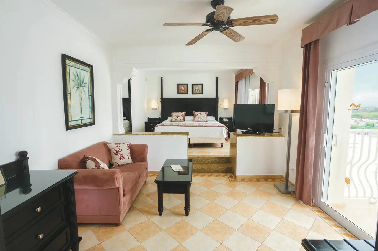Elegant suite at Hotel Riu Palace Antillas with king bed, plush couch, TV, and balcony view.